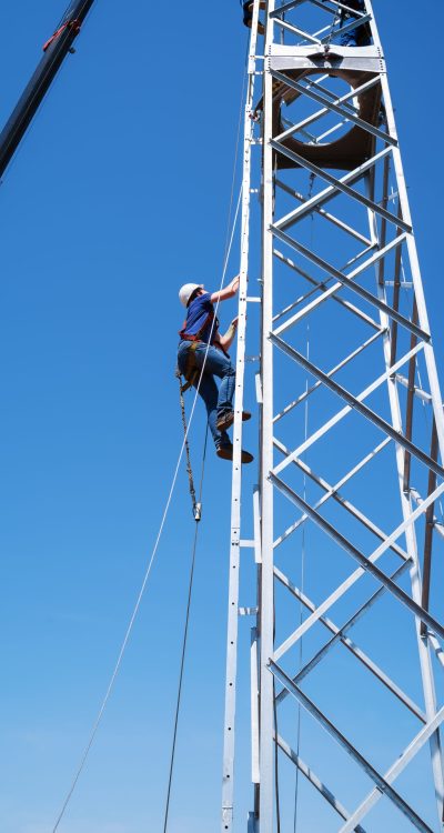 A fitter climbs the stairs of a wind turbine truss tower. Installation and construction works. Photo taken on a sunny summer day in Russia